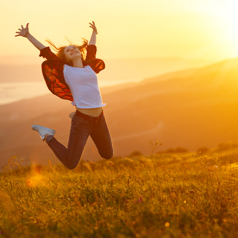 A woman jumping joyfully in front of a mountainous landscape, capturing the sense of freedom, gratitude, and happiness.