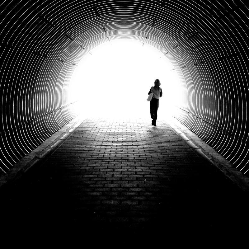 A silhouette of a person walking through a circular tunnel toward a bright light, symbolizing hope and navigating uncertainty.