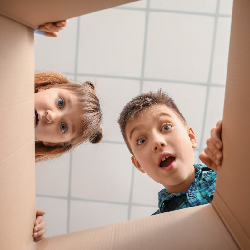 Two curious children looking into a cardboard box with expressions of wonder, uncertainty and surprise, symbolizing the excitement and creativity that arise from the unknown.