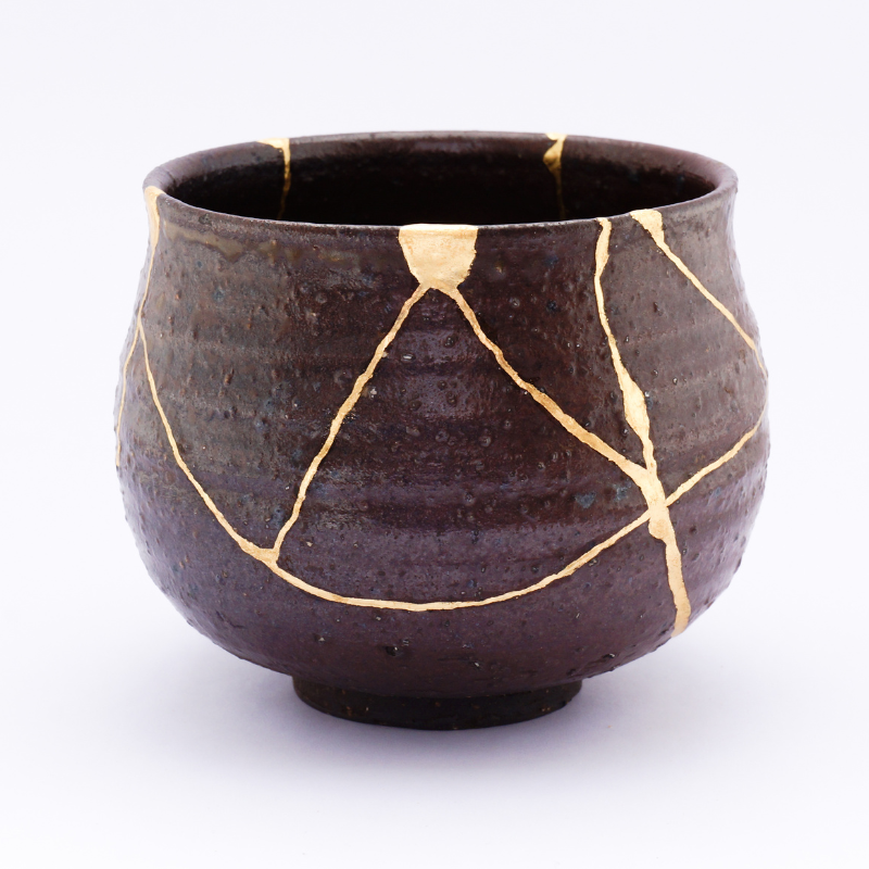 A dark ceramic bowl repaired with gold using the Japanese art of Kintsugi, symbolizing resilience, transformation, and embracing imperfections.