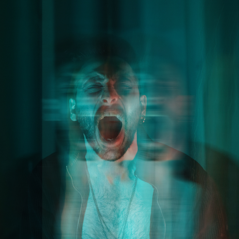 A distressed man screams with his mouth wide open, surrounded by motion blur, creating a ghostly, fragmented effect—symbolizing emotional overwhelm and the isolating intensity of anger he feels.