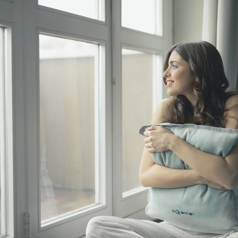 Woman looking out the window with a soft smile, finding peace in a quiet moment