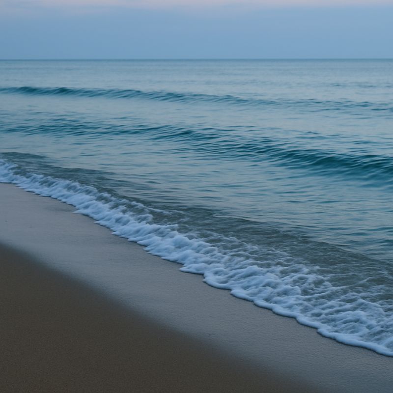 Gentle ocean waves lapping quietly at a sandy shore at dusk